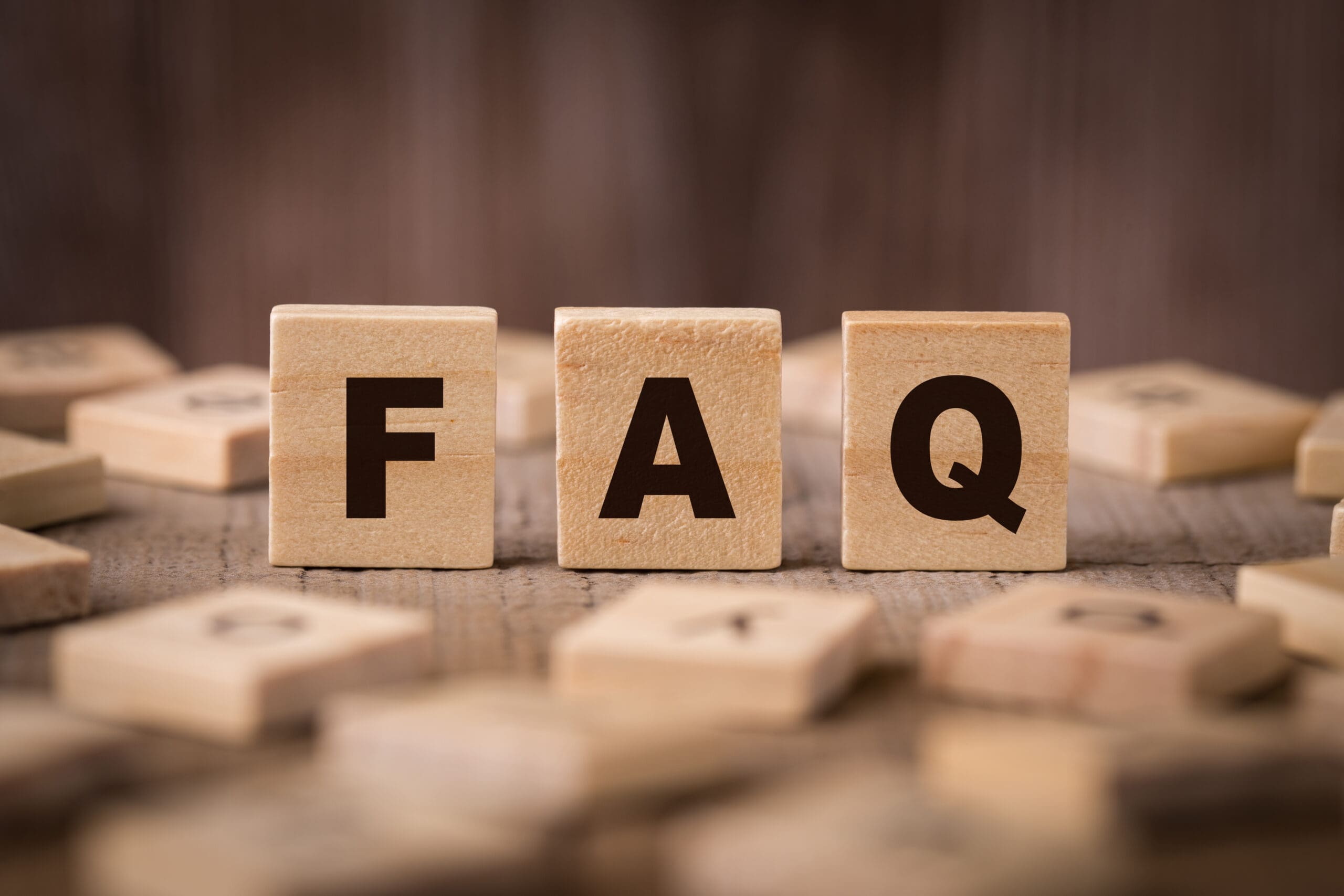 Wooden blocks with the letters "F", "A", and "Q" are arranged side by side on a wooden surface, with other scattered lettered blocks blurred in the background.